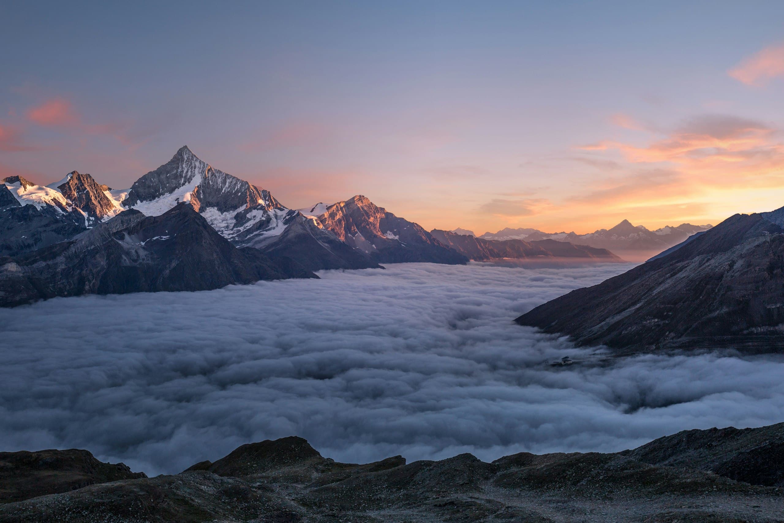 Sunrise alpenglow on snow-capped peaks above a sea of clouds